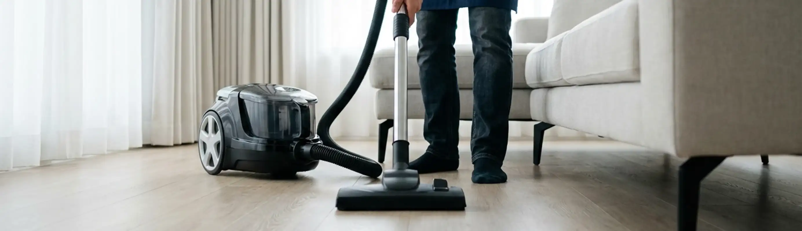 Professional house cleaner vacuuming a living room floor with a canister vacuum cleaner, Nashua, NH.