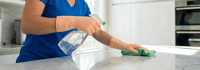 Maid service worker spraying and wiping a kitchen countertop with a microfiber cloth for sanitizing, Nashua, NH.
