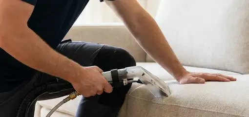 Professional upholstery cleaner deep-cleaning a fabric sofa with a handheld extraction tool, Nashua, NH.