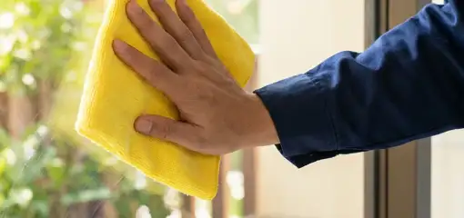 House cleaner wiping a glass window with a yellow microfiber cloth for streak-free cleaning, Nashua, NH.
